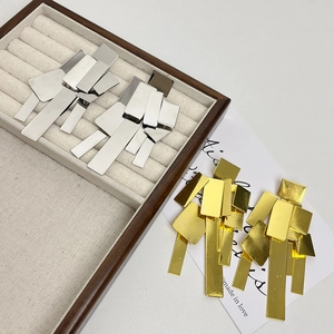 Macro shot of silver and gold geometric layered metal earrings on wooden jewelry tray
