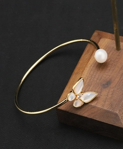 Detail of a golden open bracelet featuring a shell butterfly and a white pearl on wood stand