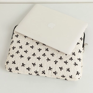 Macro detail of quilted cream laptop sleeve with black bow print and metal zipper closure