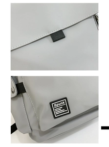 Detail of grey fabric backpack showing precise stitching, logo patch and flap closure