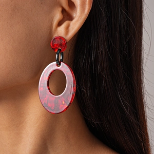 Close-up of red marble pattern acrylic oval hoop earring worn by a model
