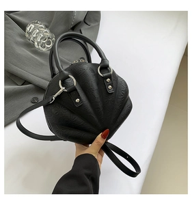 Detailed view of black shell-shaped handbag with textured leather and dual handles