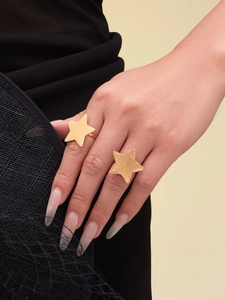 Detailed view of two oversized matte gold star rings on fingers with a mesh fabric backdrop