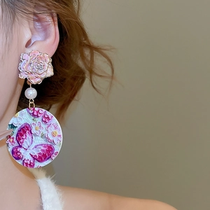 Close-up of floral butterfly pendant earrings featuring a pink rose and pearl detail