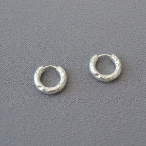 Detailed macro shot of silver-tone hoop earrings with hammered texture on grey fabric