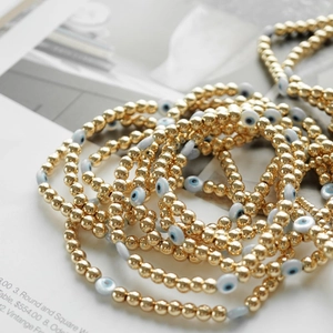 Macro shot of stacked 18K gold-plated beaded bracelets with blue evil eye charms