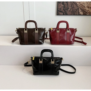 Three glossy crossbody bags in dark brown, wine red, and black on a white display stand