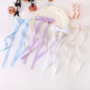 Detailed close-up of colorful satin bow hair clips in light blue, purple, white and cream