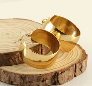 Detalle macro de pendientes de aro dorados anchos con acabado pulido en madera