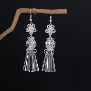 Detailed close-up of ethnic silver tassel earrings with flower hollow design on wood