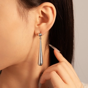 Detail of silver drop earrings with a high-polished metallic finish on a female model