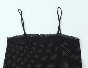 Detail van zwarte camisole met witte stippen en fijn zwart kant aan de halslijn