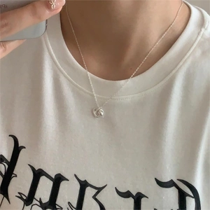 Close-up of a minimalist silver heart pendant necklace worn on a model in a casual style