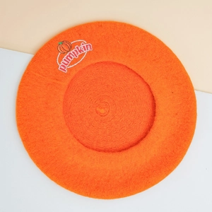 Detail der orangefarbenen Wollbaskenmütze mit weißer Kürbis-Stickerei und Text
