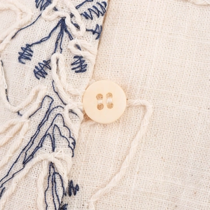 Close-up of beige linen V-neck top with floral embroidery and round button detail