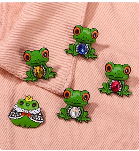 Macro shot of green enamel frog pins with colorful crystals on pink fabric texture
