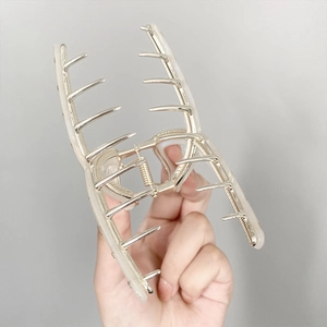Silver metal claw hair clip in sleek shark shape held against a grey background