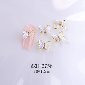 Macro detail of rotating pink crystal butterfly nail charms with gold trim and rhinestones
