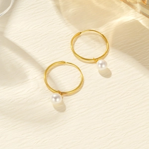 Detailed view of large gold hoop earrings with white round pearl pendants on textured fabric