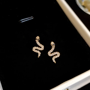 Macro shot of gold snake earrings with inlaid zircons on a black velvet background