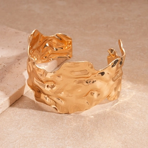 Bracelet manchette doré large avec texture martelée irrégulière sur un socle en pierre