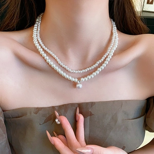 Detail einer eleganten doppellagigen weißen Perlenkette mit Strassanhänger am Model