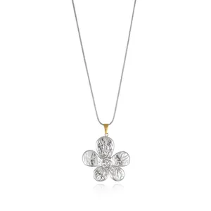 Macro detail of textured silver flower pendant with gold bail on sleek snake chain