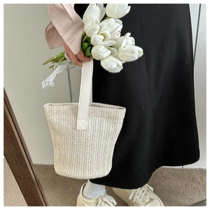 Detail of beige woven straw bucket bag with reinforced stitching and handle texture