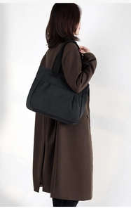 Back view of a large black canvas tote bag with wide straps worn by a model in casual style