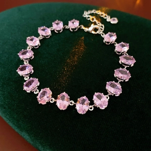 Close-up of pink oval-cut zircon bracelet with lobster clasp on dark green velvet