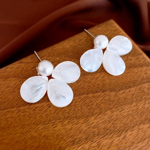 Detailed macro shot of white flower pearl stud earrings on a wooden display stand