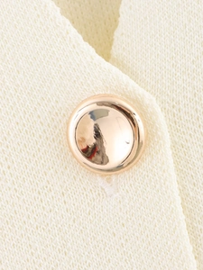 Detailaufnahme von cremefarbenem Strickstoff mit einem polierten goldenen Metallknopf