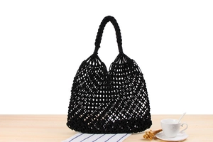 Close-up of black handmade macrame woven tote bag with thick braided handles on wood