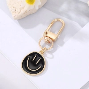 Close-up of a golden mini smiley face pendant keychain with black enamel details