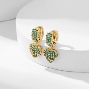Golden heart earrings with micro-paved green zircons shown on a white geometric stand