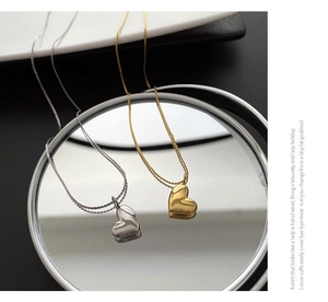 Close-up of gold and silver heart necklaces reflecting on a mirror surface