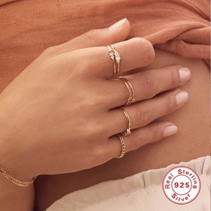 Close-up of stacked 925 sterling silver gold rings and zircon jewelry on a hand