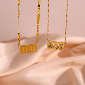 Detail of gold 11:11 rectangle pendants on pig nose chains over pink satin fabric