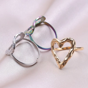 Three hammered heart rings in gold, silver, and rainbow steel on pink silk background
