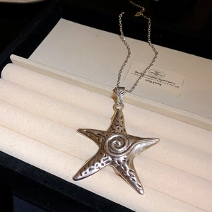 Macro shot of a silver starfish pendant with spiral texture on a beige jewelry box