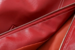 Macro detail of red faux leather jacket featuring metal zipper and white contrast stitching