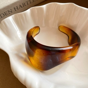 Macro shot of amber resin open cuff bracelet with tortoiseshell texture in a shell dish