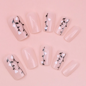 Detail shot of light pink press-on nails with minimalist black vine and white heart patterns