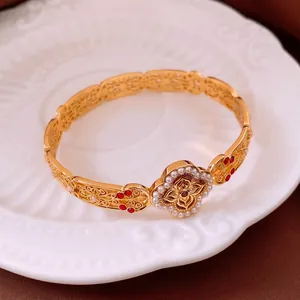 Vintage gold filigree bangle with pearls and red stones on a white ceramic plate