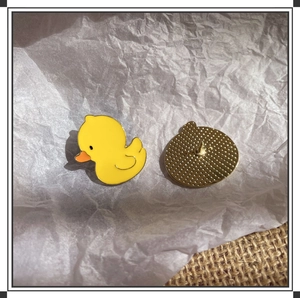 Cute yellow duckling metal pins with vibrant orange beaks on white textured background