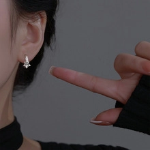 Close-up of a silver star-shaped earring with zircon inlays worn on a model's earlobe