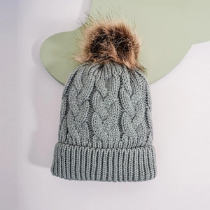 Close-up of gray cable-knit texture and large dark brown faux fur pompom on winter hat