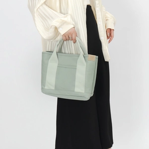 Detail of light green canvas tote bag showing the front pocket and textured strap