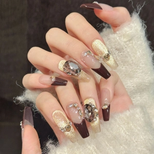 Macro detail of coffin-shaped caramel nails with gems, glitter, and pearl accents