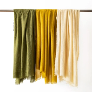 Detail view of cotton linen scarves in military green, mustard yellow, and beige with fringes